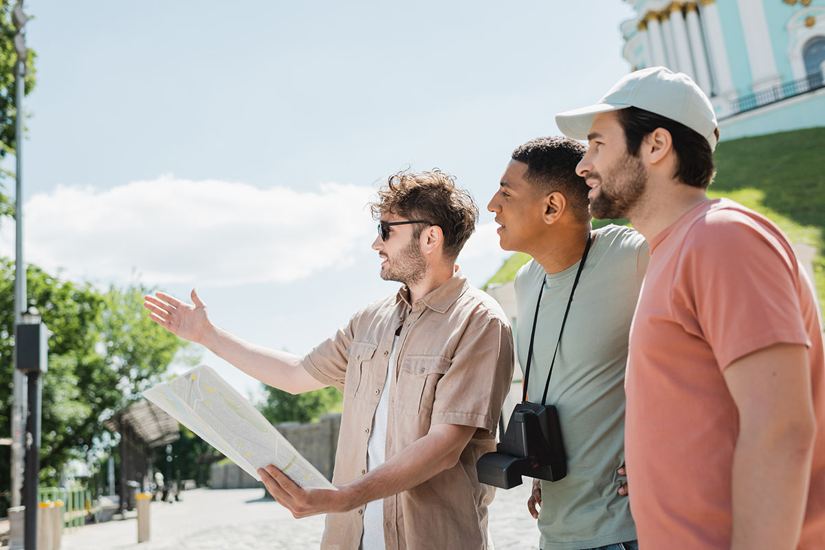 A tour guide with a map is pointing into the distance while two tourists with cameras look onward.