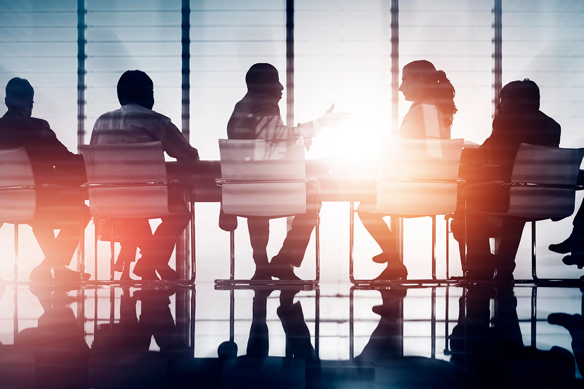 Silhouettes of six individuals seated around a conference table, with sunlight streaming through large windows, creating a dramatic effect on the scene.